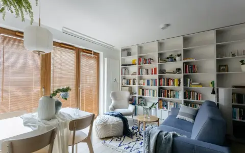 Przytulna biblioteczka w salonie z niebieską kanapą, fotelem i stolikiem.