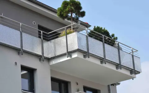 Nowoczesny balkon z ażurową balustradą i drzewkami iglastymi. Jaki spadek na balkonie, by woda deszczowa spływała?