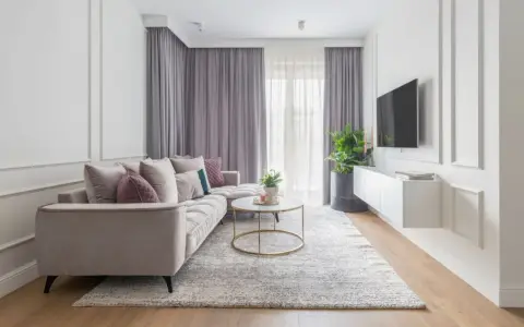 Elegancki salon w stylu modern classic. Jasna kanapa, okrągły stolik kawowy, dywan i zasłony tworzą przytulną atmosferę.