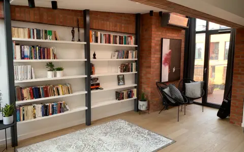 Nowoczesna biblioteczka w stylu bauhaus z ceglaną ścianą, czarnymi krzesłami i dywanem.