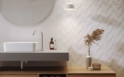 Nowoczesna łazienka z białymi płytkami w jodełkę. Idealna fuga do białych płytek podkreśla geometryczny wzór. Umywalka, lustro i drewniane meble tworzą harmonijną całość.