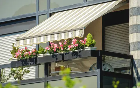 Jak zrobić daszek na balkon? Płócienny markiza chroni przed słońcem, a skrzynki z kwiatami dodają uroku.