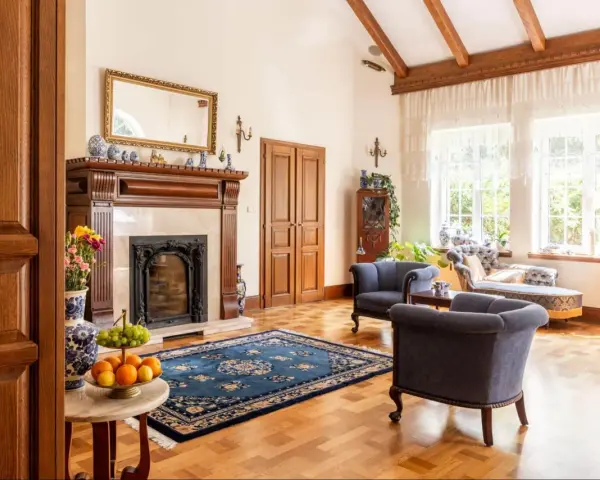 Elegancki salon w stylu kolonialnym z kominkiem, drewnianymi belkami stropowymi i stylowymi meblami.