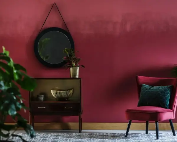 Eleganckie wnętrze w kolorze marsala, z aksamitnym fotelem, lustrem i roślinami.