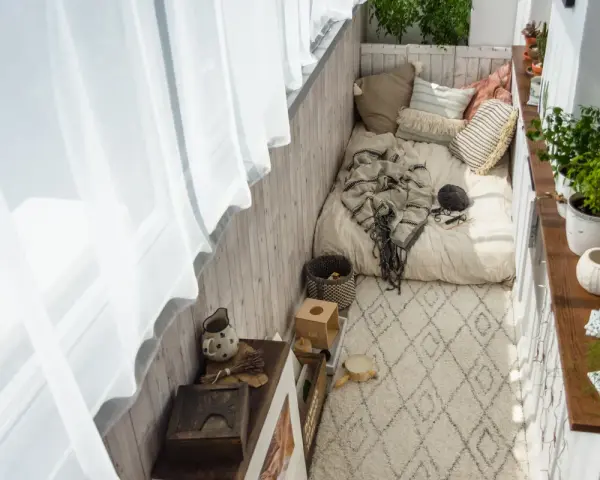 Przytulny balkon w stylu boho: łóżko z kocem, poduszki, dywan, rośliny i drewniane dekoracje. Idealne inspiracje na relaks.
