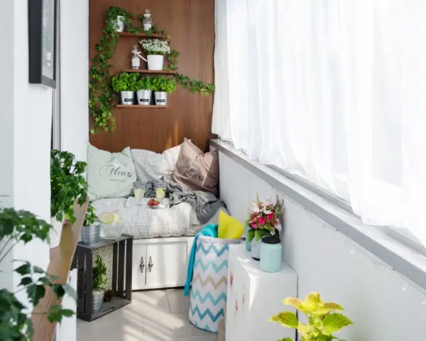Przytulny balkon typu loggia z wygodną kanapą, ziołami na drewnianej ścianie i bukietem kwiatów. Idealne miejsce na relaks.