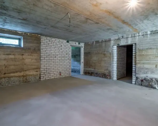 Surowa piwnica ziemna z betonowymi ścianami, białymi ceglanymi wstawkami i oknem. Widać przygotowania do wentylacji piwnicy ziemnej.