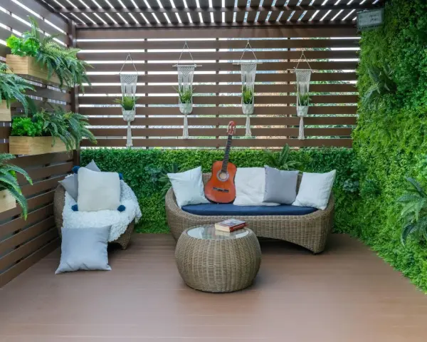 Zielony, bujny balkon w bloku z rattanowymi meblami, gitarą i książką. Idealne miejsce na relaks.