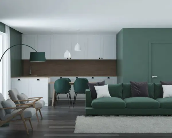Nowoczesny salon z kuchnią, gdzie dominują zielony kolor ścian i mebli. Wygodna sofa, fotele i stół z krzesłami tworzą przytulną przestrzeń.