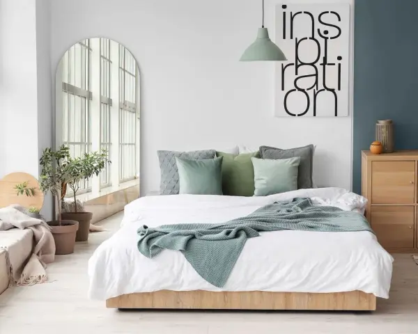 Sypialnia inspiracje kolory: zielone poduszki i pled na białej pościeli, łóżko z drewnianą ramą, duże lustro, rośliny i obraz z napisem "inspiration".