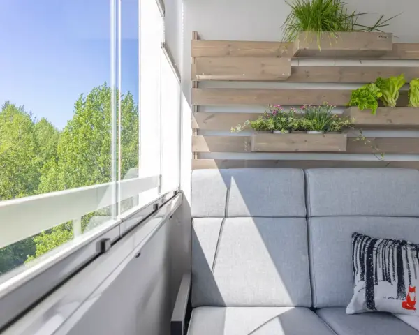 Przytulny mały balkon w bloku z szarą sofą, poduszką z liskiem i zielenią na drewnianej ściance.