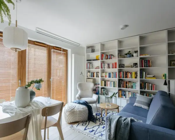 Przytulna biblioteczka w salonie z niebieską kanapą, fotelem i stolikiem.