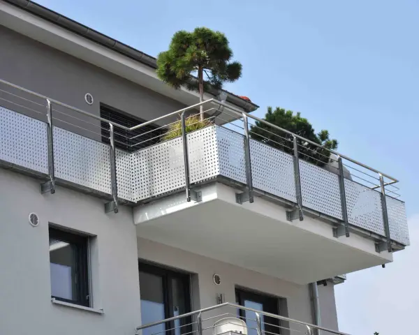 Nowoczesny balkon z ażurową balustradą i drzewkami iglastymi. Jaki spadek na balkonie, by woda deszczowa spływała?