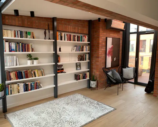 Nowoczesna biblioteczka w stylu bauhaus z ceglaną ścianą, czarnymi krzesłami i dywanem.