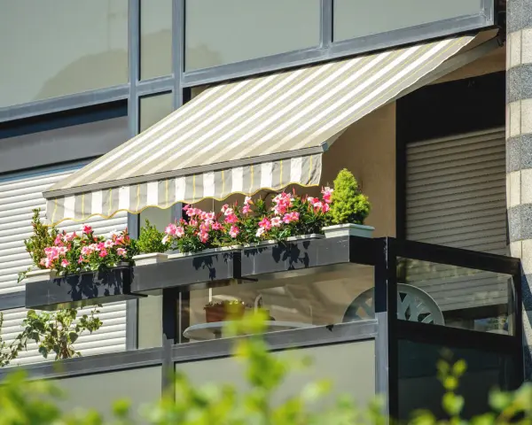 Jak zrobić daszek na balkon? Płócienny markiza chroni przed słońcem, a skrzynki z kwiatami dodają uroku.