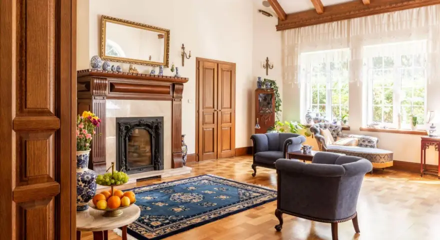 Elegancki salon w stylu kolonialnym z kominkiem, drewnianymi belkami stropowymi i stylowymi meblami.