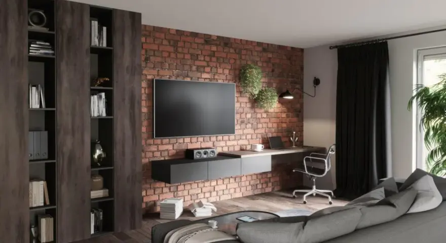 Nowoczesny salon loft inspiracje: ceglana ściana, wisząca szafka RTV, biurko z laptopem, regały i szara kanapa.