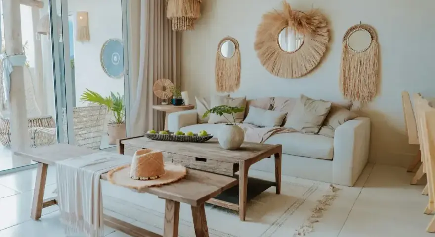 Przytulny salon w stylu bohema. Jasna sofa, drewniane meble, plecione dekoracje i słomkowy kapelusz tworzą relaksującą atmosferę.