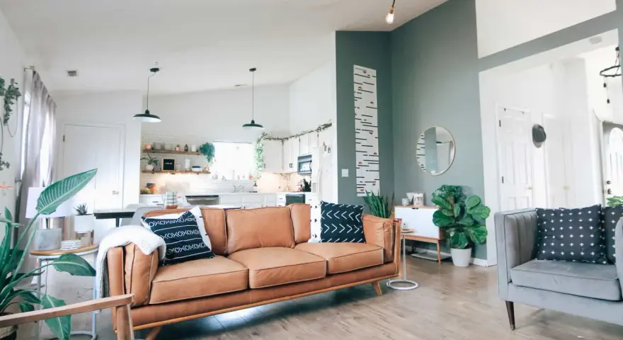 Nowoczesny salon z brązową kanapą i szarym fotelem. Ściana w kolorze zielonym dodaje charakteru, a rośliny wprowadzają życie. Idealny kolor do salonu.