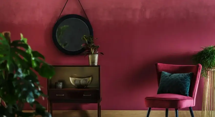 Eleganckie wnętrze w kolorze marsala, z aksamitnym fotelem, lustrem i roślinami.