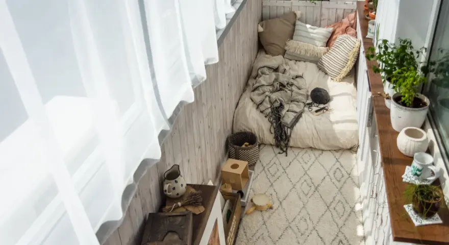 Przytulny balkon w stylu boho: łóżko z kocem, poduszki, dywan, rośliny i drewniane dekoracje. Idealne inspiracje na relaks.