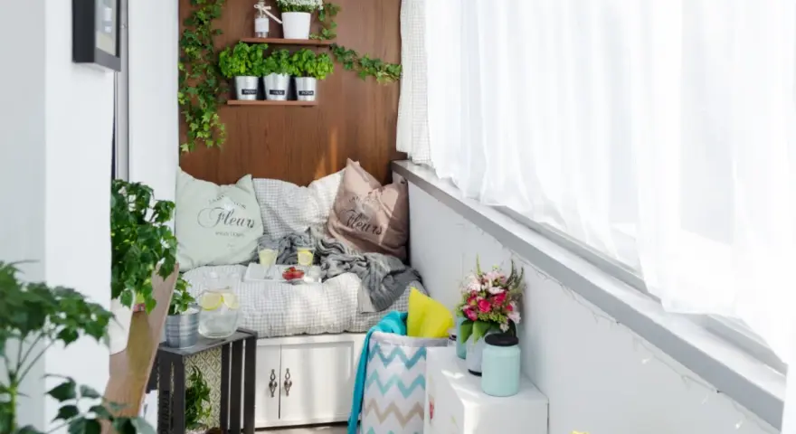 Przytulny balkon typu loggia z wygodną kanapą, ziołami na drewnianej ścianie i bukietem kwiatów. Idealne miejsce na relaks.
