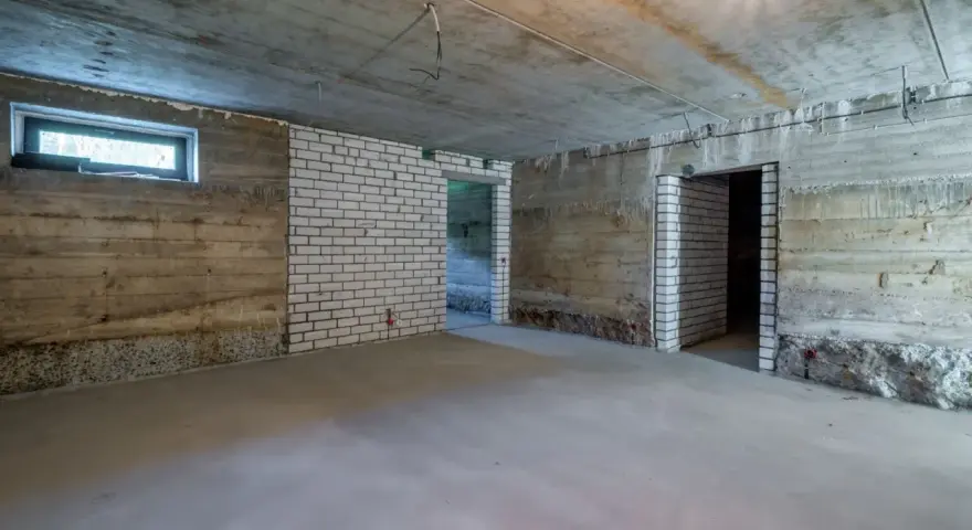 Surowa piwnica ziemna z betonowymi ścianami, białymi ceglanymi wstawkami i oknem. Widać przygotowania do wentylacji piwnicy ziemnej.