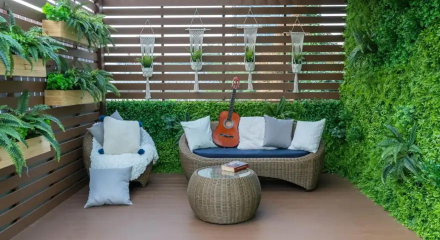 Zielony, bujny balkon w bloku z rattanowymi meblami, gitarą i książką. Idealne miejsce na relaks.