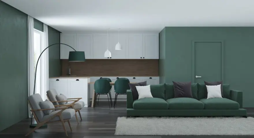 Nowoczesny salon z kuchnią, gdzie dominują zielony kolor ścian i mebli. Wygodna sofa, fotele i stół z krzesłami tworzą przytulną przestrzeń.