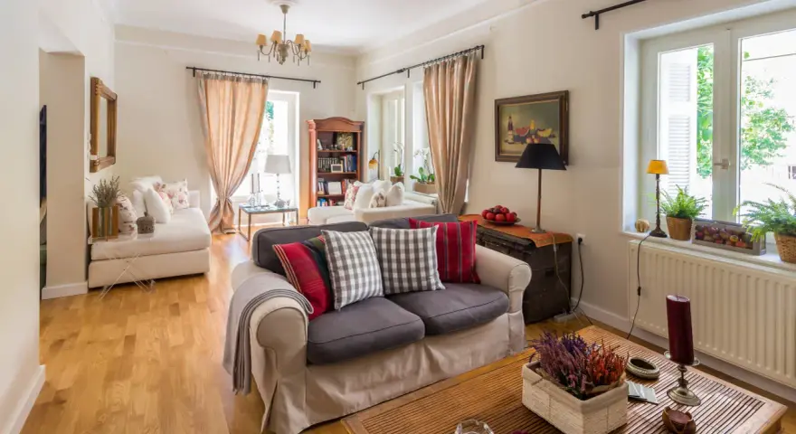 Przytulny salon w stylu angielskim nowoczesnym. Jasne ściany, drewniana podłoga, wygodne sofy z poduszkami w kratę i paski.