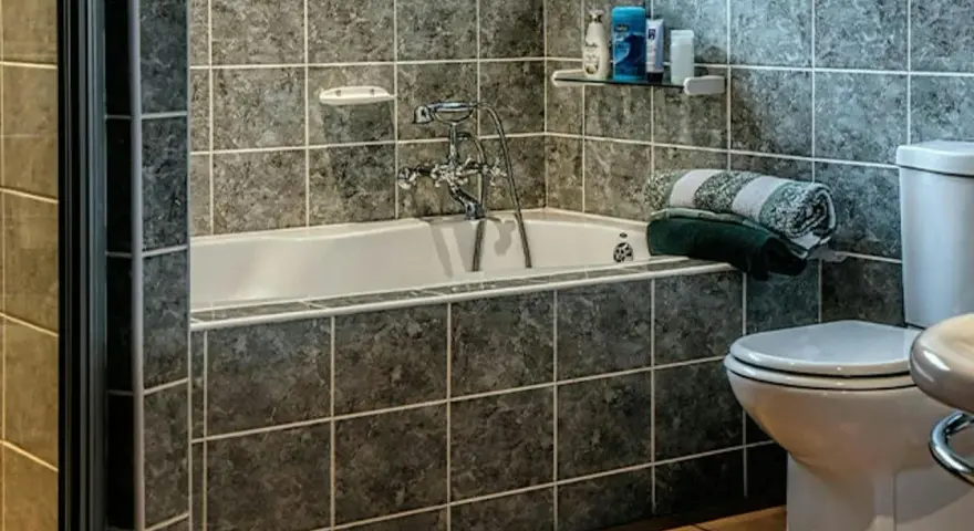 Łazienka z wanną i toaletą, ściany wyłożone ciemnymi, marmurkowymi kaflami. Planowanie malowania kafelek w łazience.
