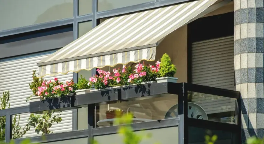 Zadaszenie balkonu z markizą i kwitnącymi kwiatami to świetny sposób, jak osłonić balkon przed słońcem i deszczem.