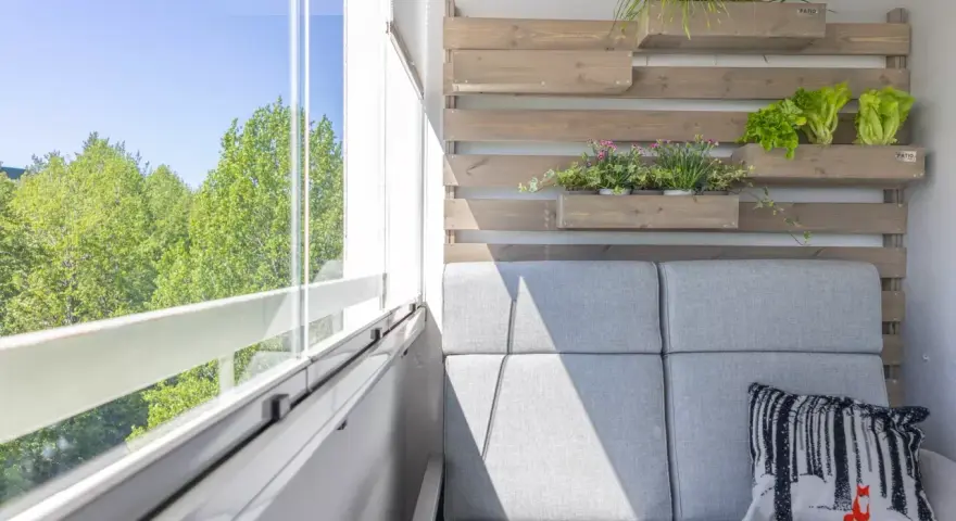 Przytulny mały balkon w bloku z szarą sofą, poduszką z liskiem i zielenią na drewnianej ściance.