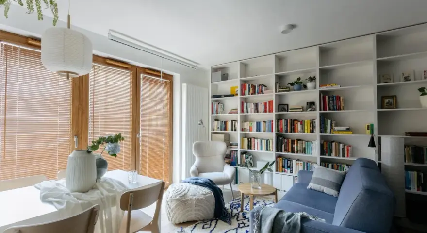 Przytulna biblioteczka w salonie z niebieską kanapą, fotelem i stolikiem.
