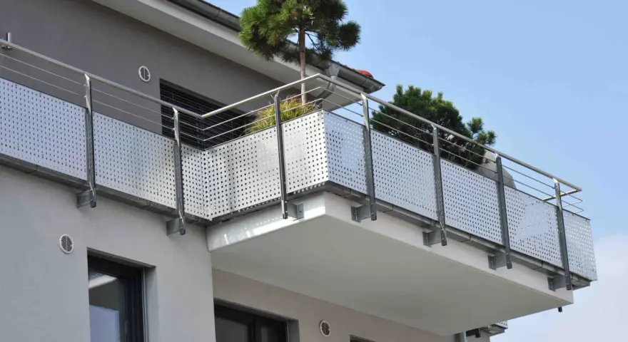 Nowoczesny balkon z ażurową balustradą i drzewkami iglastymi. Jaki spadek na balkonie, by woda deszczowa spływała?