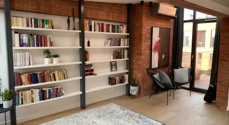 Nowoczesna biblioteczka w stylu bauhaus z ceglaną ścianą, czarnymi krzesłami i dywanem.