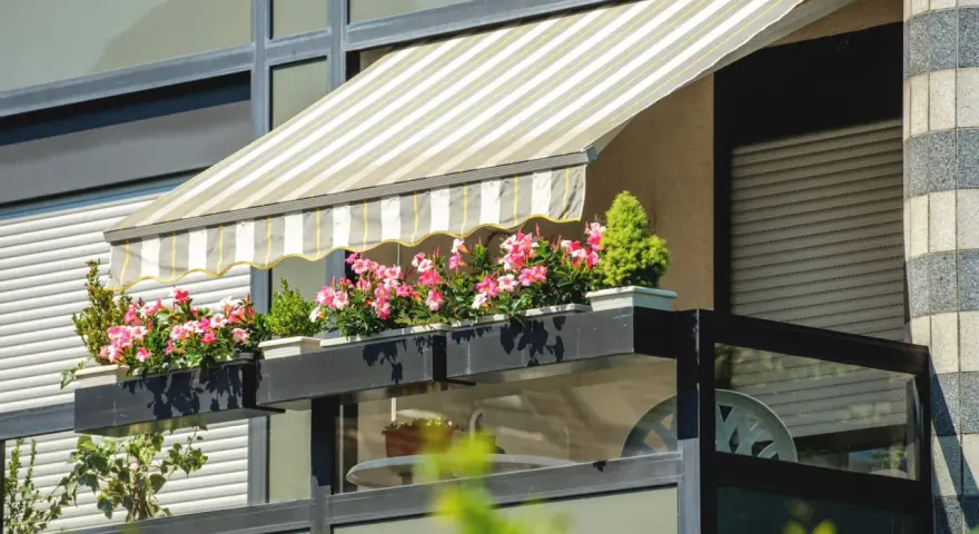 Jak zrobić daszek na balkon? Płócienny markiza chroni przed słońcem, a skrzynki z kwiatami dodają uroku.