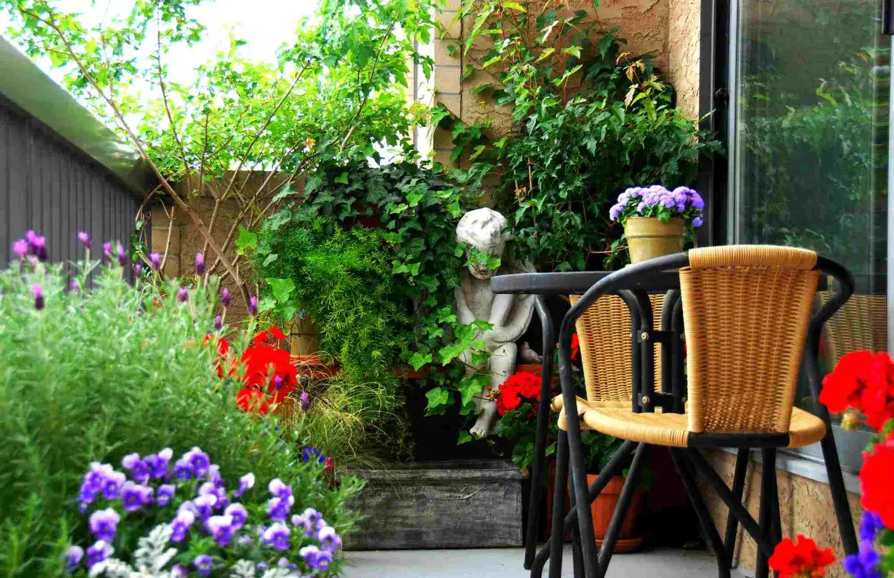 Balkon inspiracje: uroczy zakątek z rzeźbą aniołka, wiklinowym fotelem i mnóstwem zieleni.