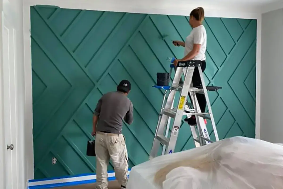Para malowania ścian inspiracje: para maluje zieloną ścianę z geometrycznym wzorem.