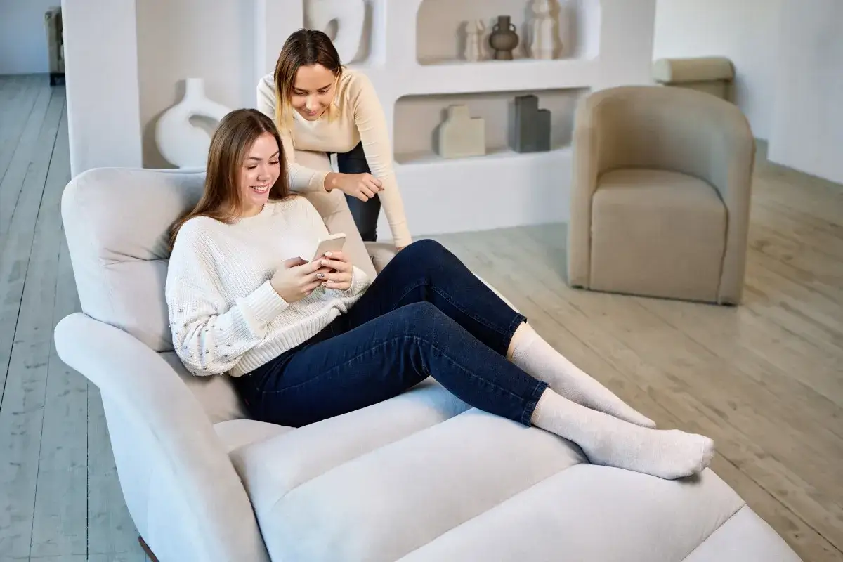Dwie kobiety relaksują się na wygodnym szezlongu, jedna przegląda telefon.