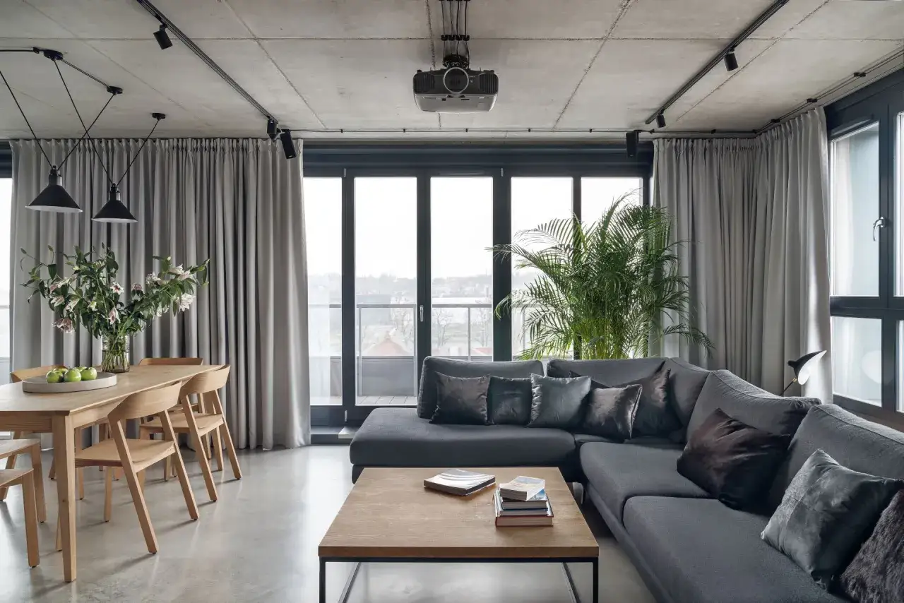 Nowoczesny salon loft inspiracje: szara sofa, drewniany stół, betonowy sufit i duża roślina.