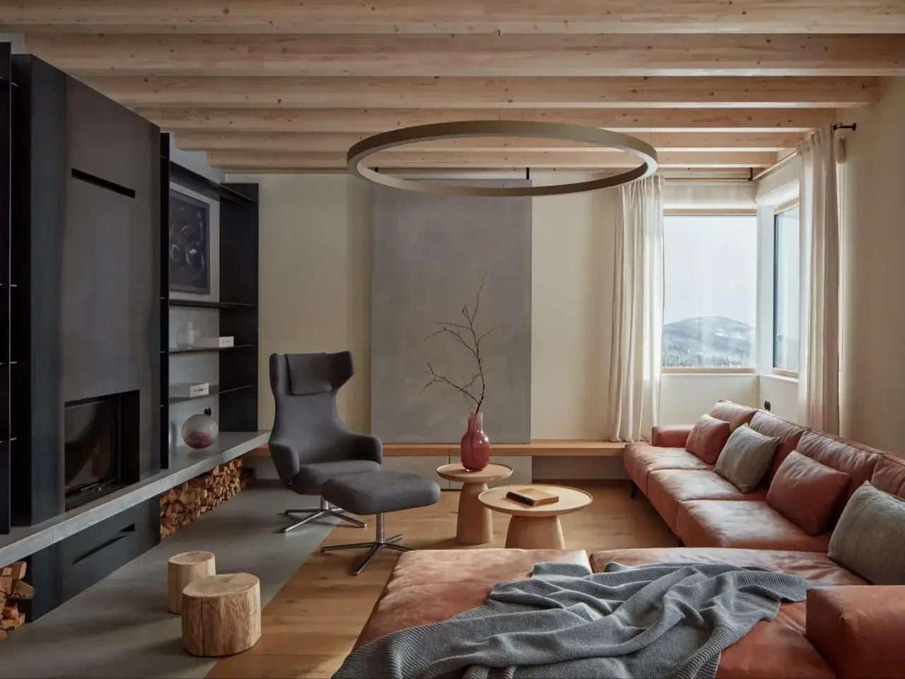 Przytulny salon w stylu modern farmhouse z wygodną, rudą kanapą, szarym fotelem i kominkiem. Drewniane belki na suficie dodają ciepła.