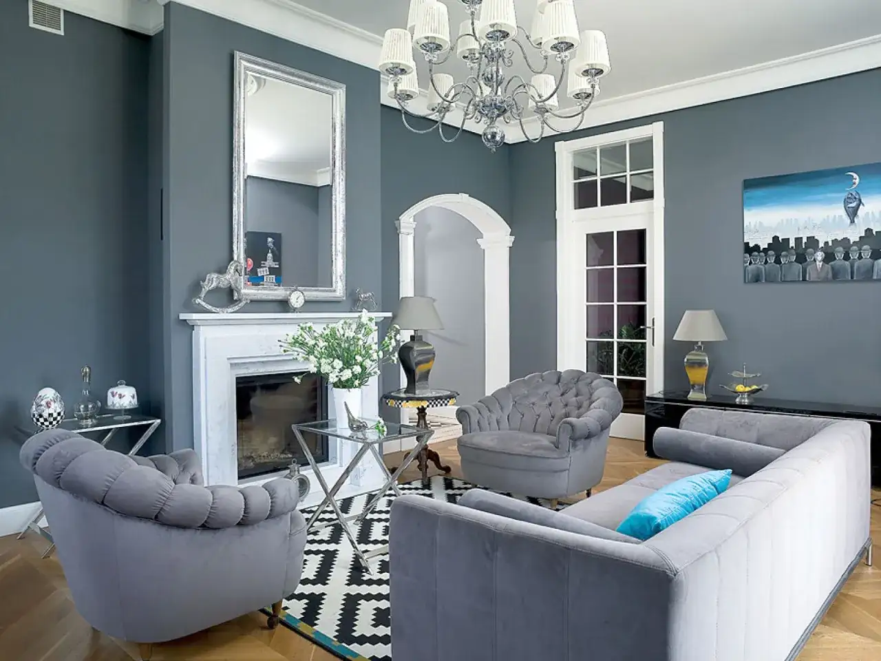 Elegancki salon w stylu angielskim nowoczesnym. Szare meble, kominek, lustro i ciekawe obrazy tworzą przytulną atmosferę.