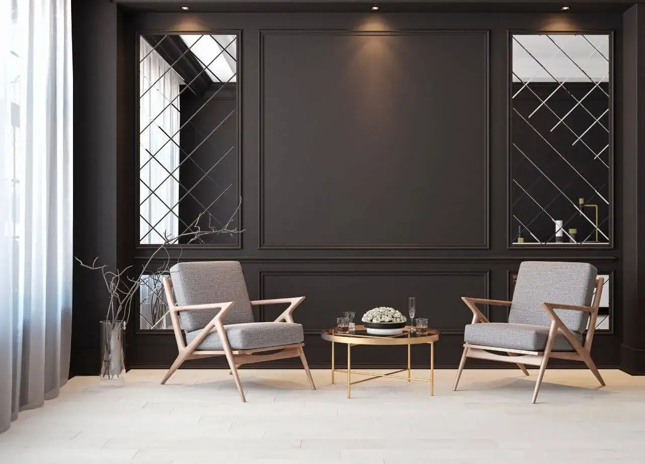 Elegancki salon z czarną ścianą, dwoma szarymi fotelami i złotym stolikiem kawowym. Lustra w romby dodają głębi.