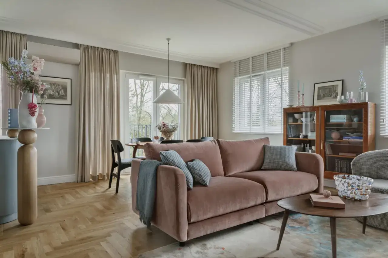 Nowoczesny salon z różową kanapą, drewnianą podłogą i stylowymi dodatkami. Inspiracja, jak pomalować salon nowocześnie, by stworzyć przytulną przestrzeń.