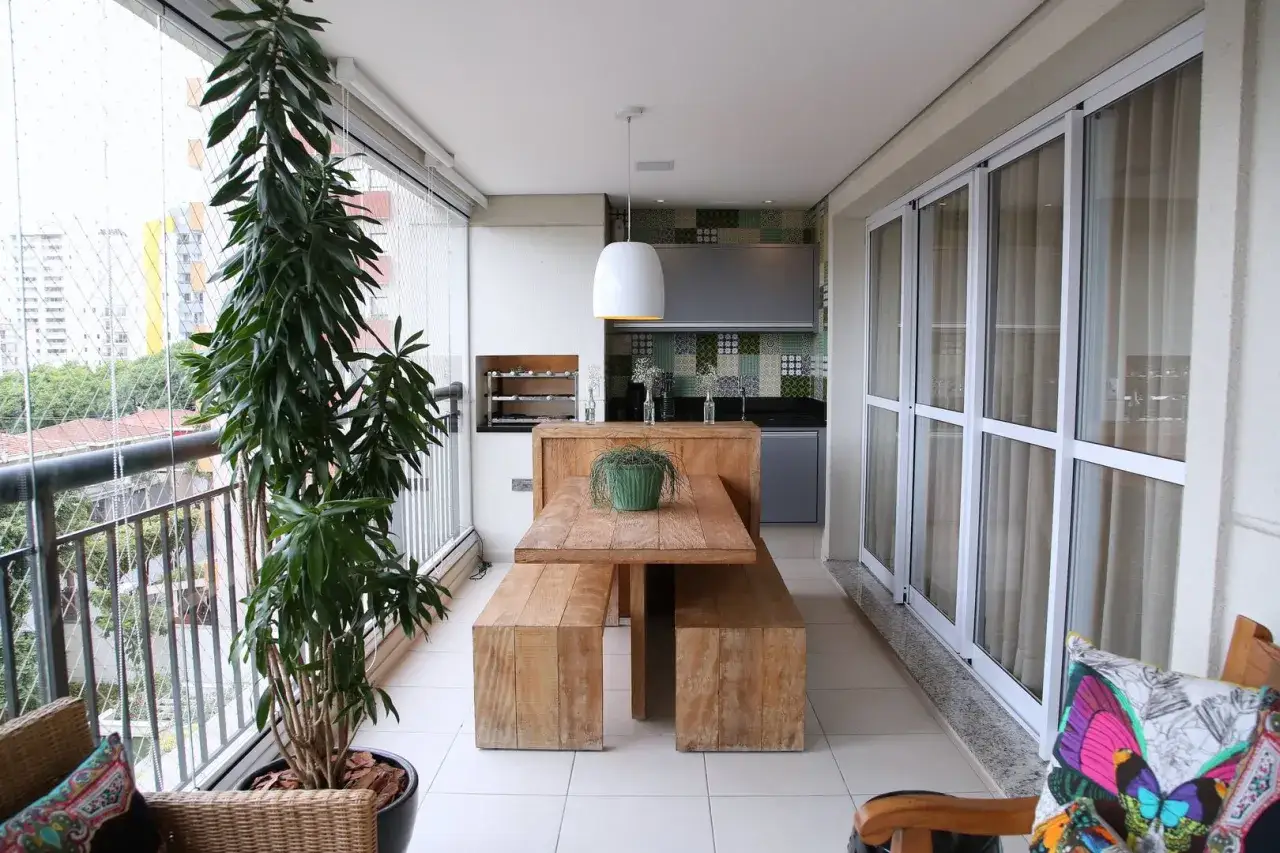 Drewniany stół z ławami i roślinnością tworzą przytulną atmosferę na balkonie typu loggia.