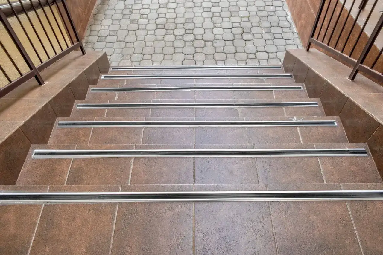 Schody zewnętrzne wyłożone brązowymi płytkami, z metalowymi listwami antypoślizgowymi. Praktyczny poradnik, jak układać płytki na schodach zewnętrznych.