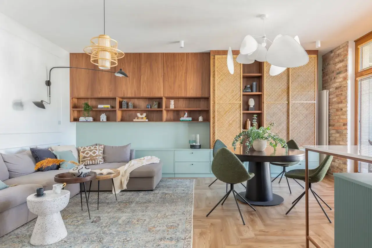 Inspiracja, jak umeblować pokój dzienny: przytulna szara sofa, drewniane meble, okrągły stół z zielonymi krzesłami i stylowe oświetlenie tworzą ciepłą atmosferę.
