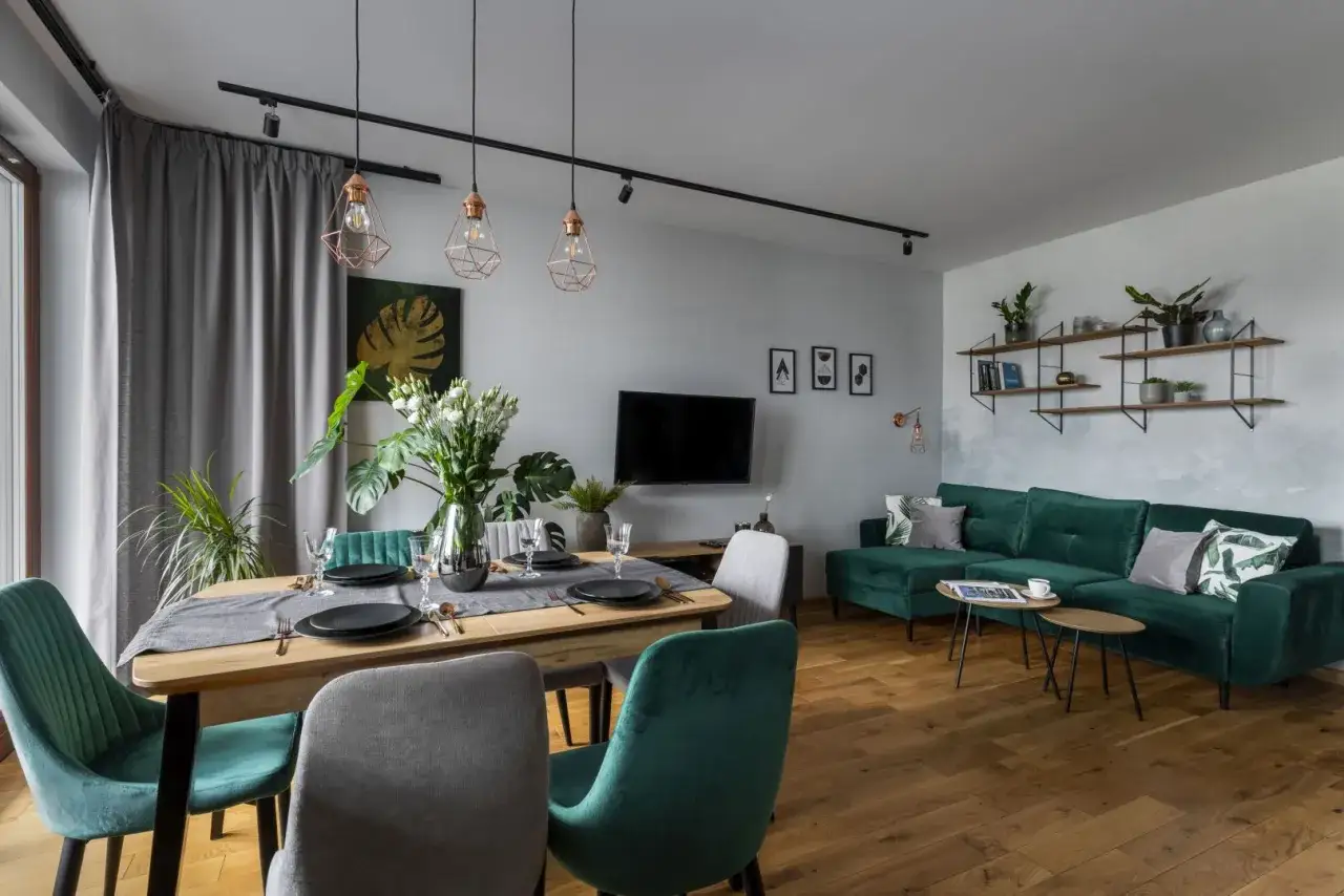 Nowoczesny salon z jadalnią. Głęboka zieleń kanapy i krzeseł nadaje wnętrzu wyrazisty kolor do salonu.