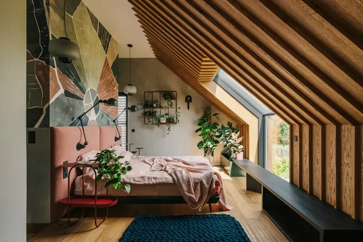 Pokój na poddaszu inspiracje: łóżko z różowym zagłówkiem, geometryczna ściana, drewniane belki i okno dachowe.